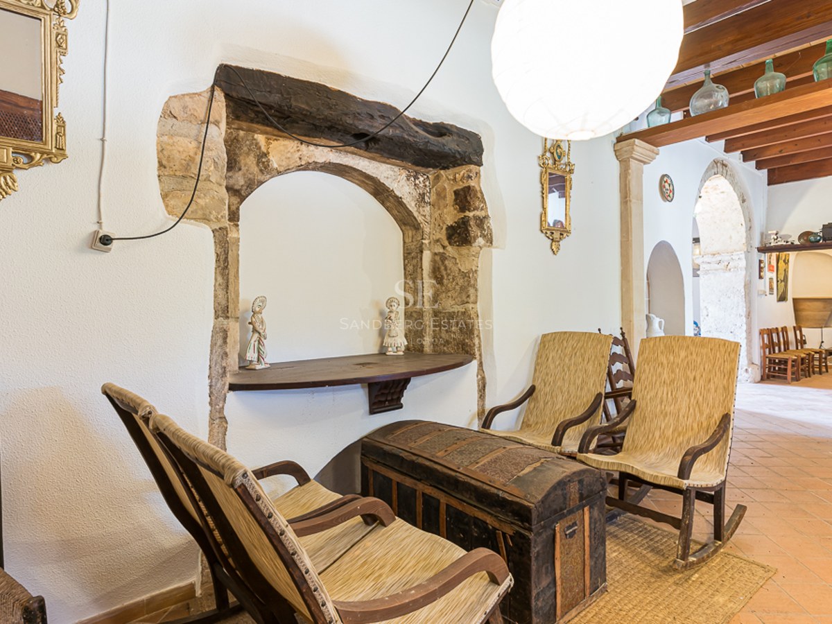 Interior with rustic rocking chairs, an antique chest, terracotta floors, and a historic stone archway.