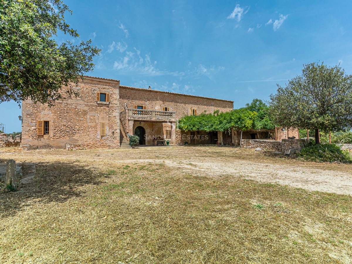 Large two-story rustic stone villa with wooden shutters and a balcony under a clear blue sky.