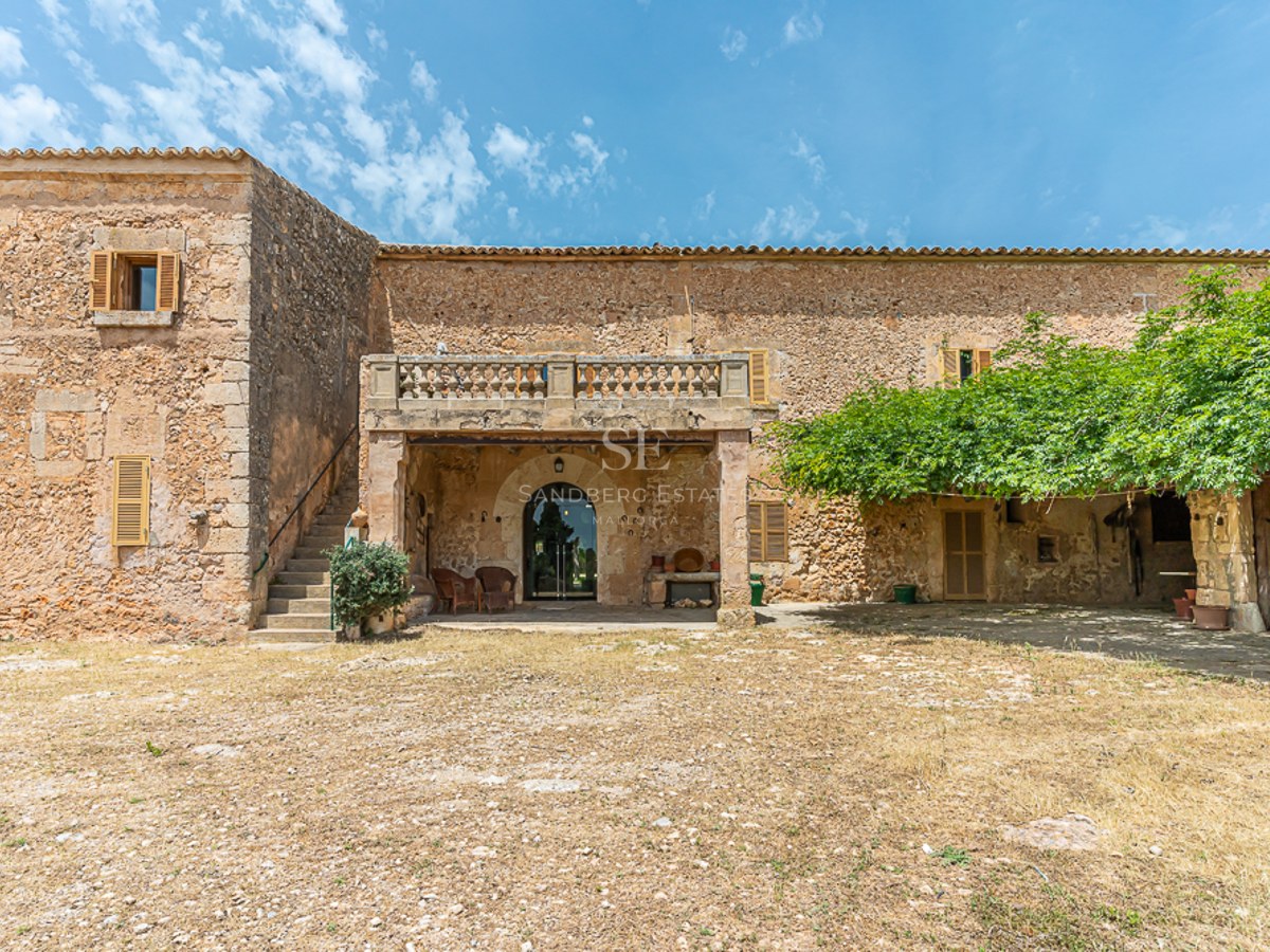 Exterior view of a rustic stone house with wooden shutters and a balcony under a bright blue sky.
