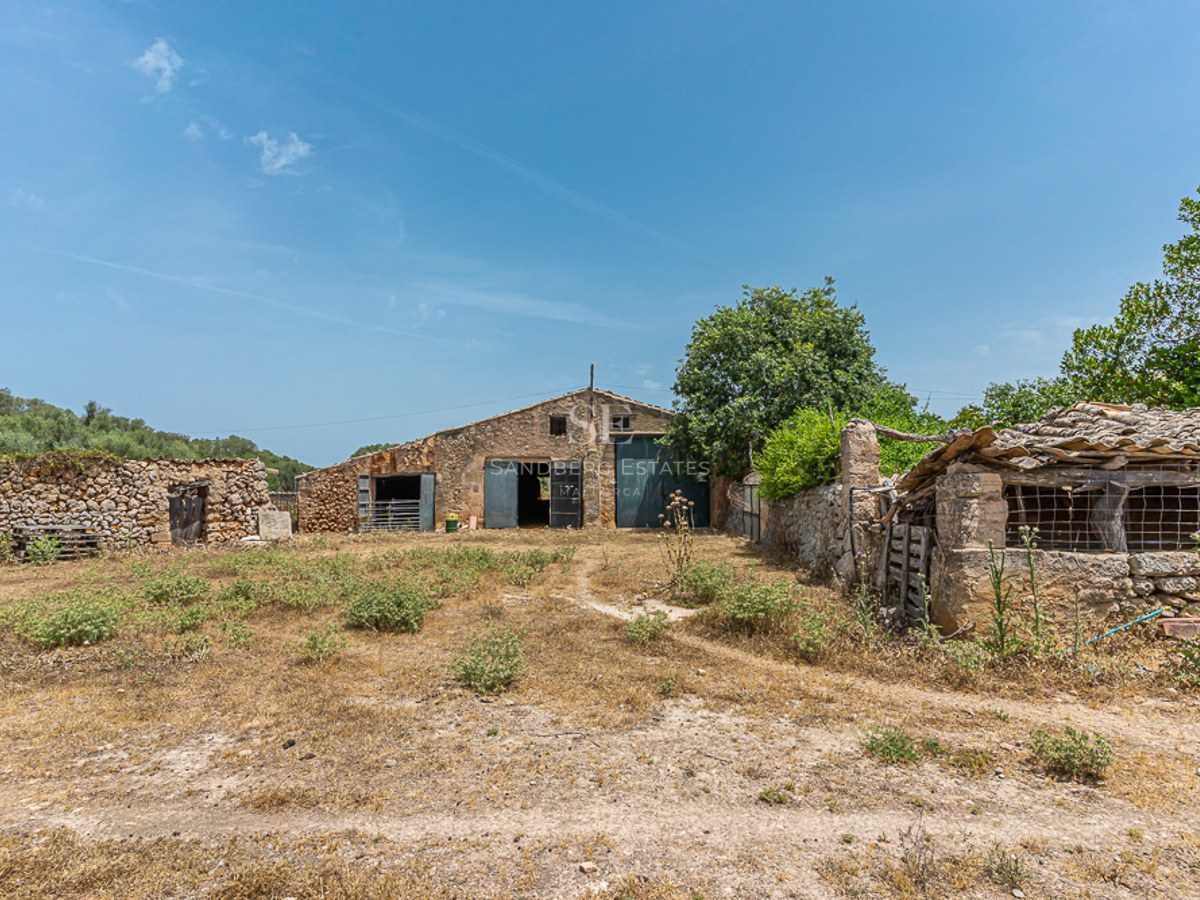 View of traditional stone buildings and dry-stone walls in a rural countryside setting under a clear blue sky.
