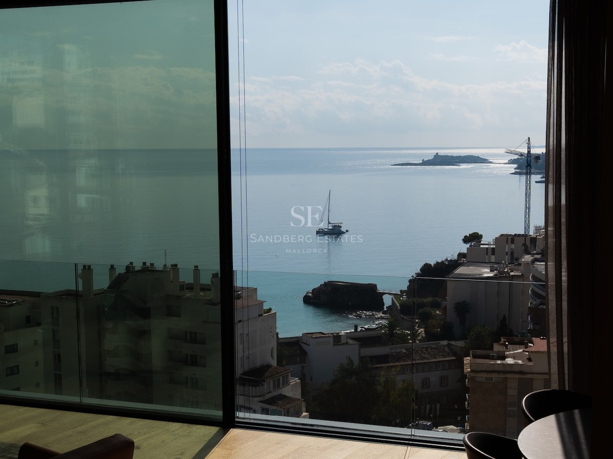 View from a modern interior through floor-to-ceiling glass looking out at the azure sea with a boat and coastline.