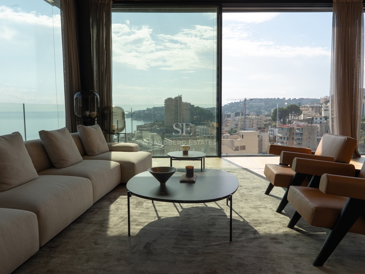Modernes Wohnzimmer mit bodentiefen Fenstern, Blick auf die Küstenstadt, beiges Sofa und Lederstühle.