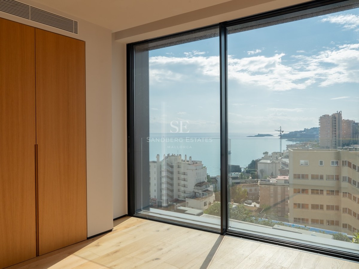 Innenansicht eines Schlafzimmers mit Eichenparkett und Einbauschränken vor einem großen Fenster mit Blick auf das Meer.