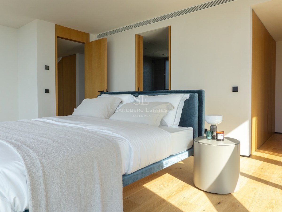 Modernes Schlafzimmer mit Eichenboden, blauem Samtbett und minimalistischen Holzelementen im Sonnenlicht.