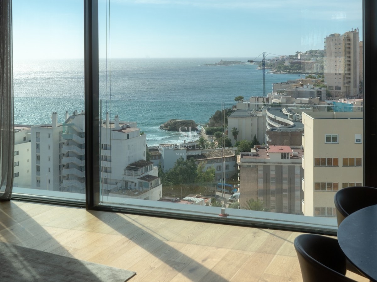Interior view through floor-to-ceiling windows showing the Mediterranean coast, blue sea, and light wood flooring.