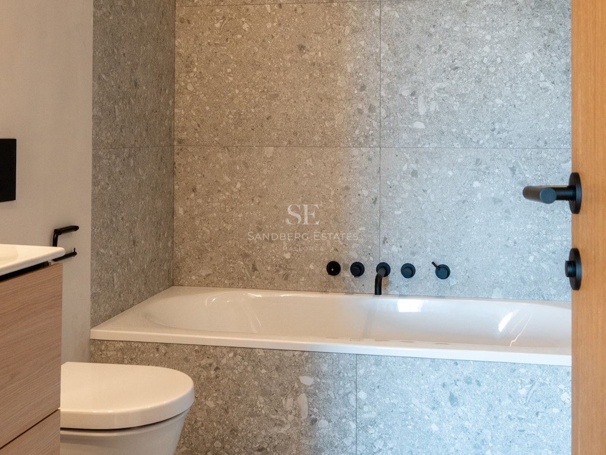 Zeitgenössisches Badezimmer mit grauen Steinfliesen, weißer Badewanne und mattschwarzen Wandarmaturen.