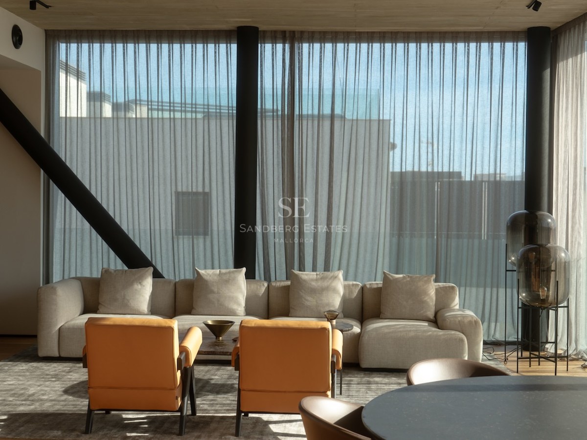 Modern living room with a large beige sofa, two tan leather armchairs, and floor-to-ceiling windows with sheer curtains.