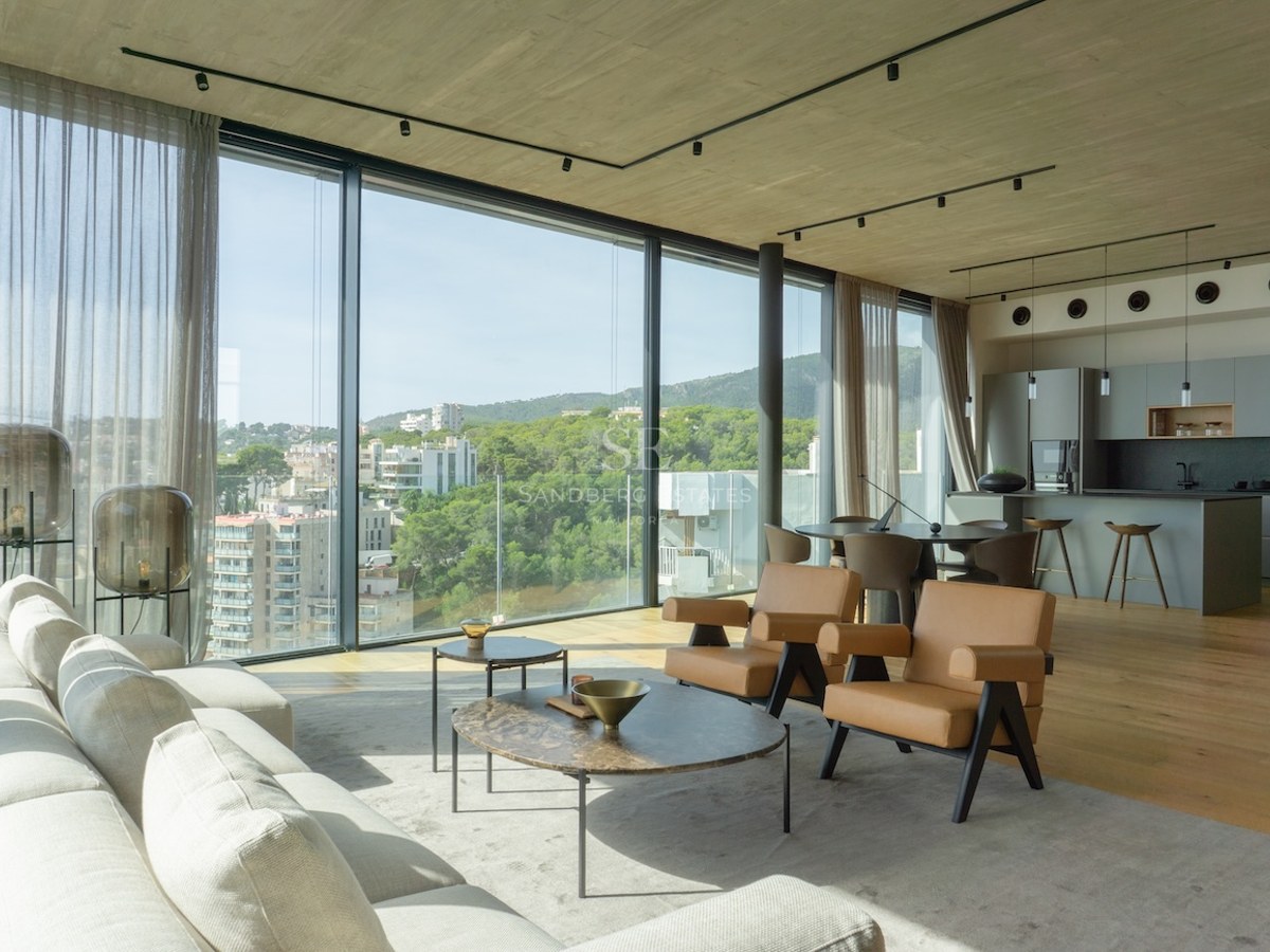 Heller Wohnraum mit bodentiefen Fenstern, Blick auf Stadt und Natur, großes graues Sofa und Designmöbel.