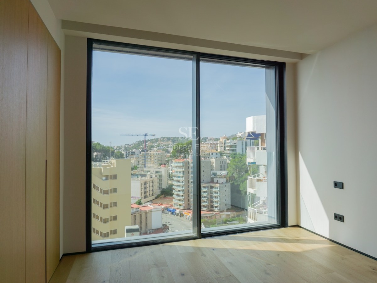 Leeres modernes Schlafzimmer mit hellen Eichenböden, Einbauschränken und einem großen bodentiefen Fenster mit Stadtblick.