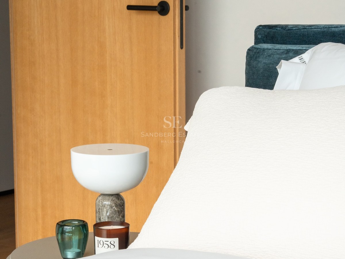 Close-up of a bed with white linens, teal velvet headboard, marble lamp, and natural oak door.