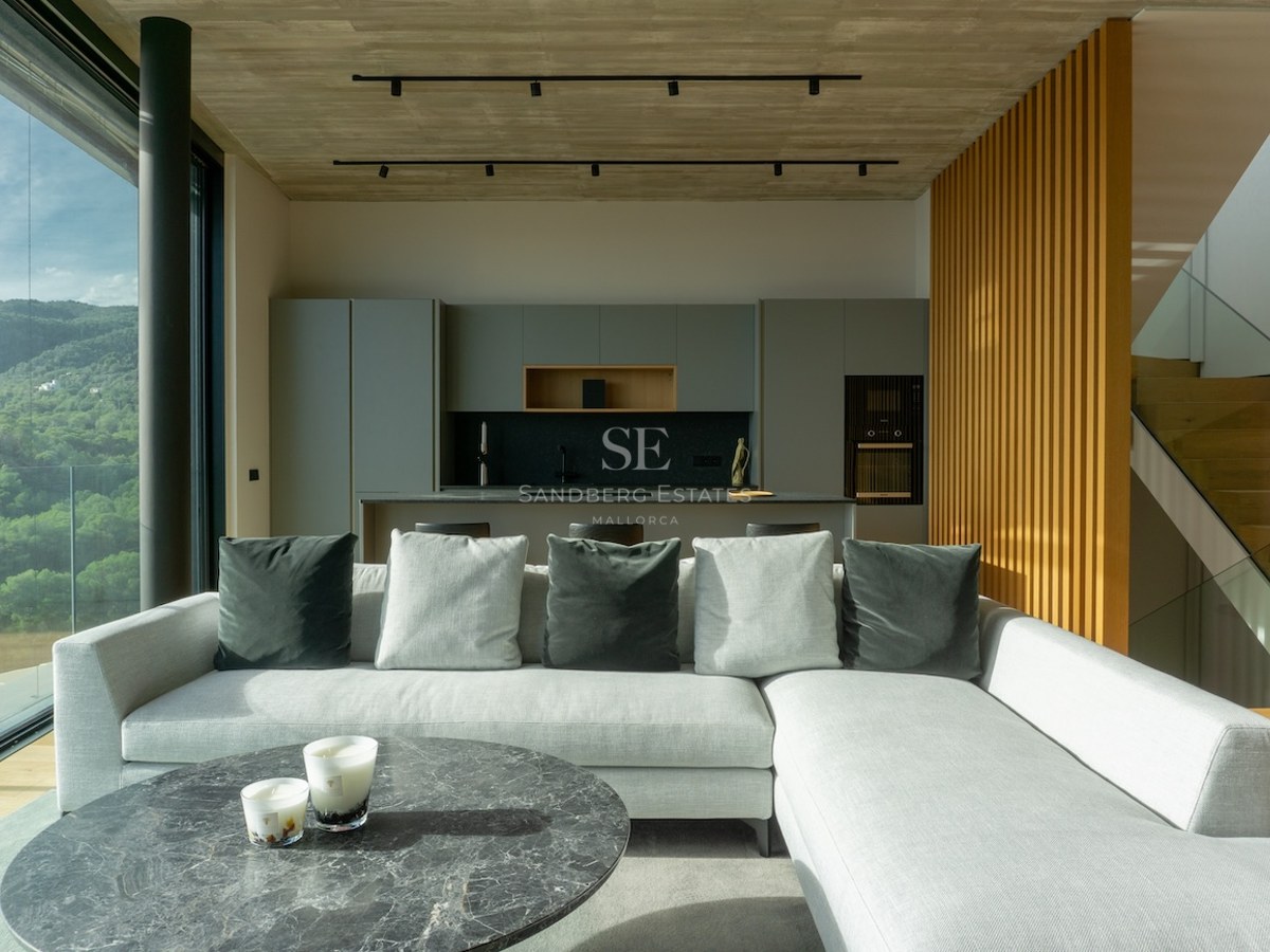 Modernes Wohnzimmer mit grauem Sofa, Marmortisch und bodentiefen Fenstern mit Blick auf grüne Hügel.
