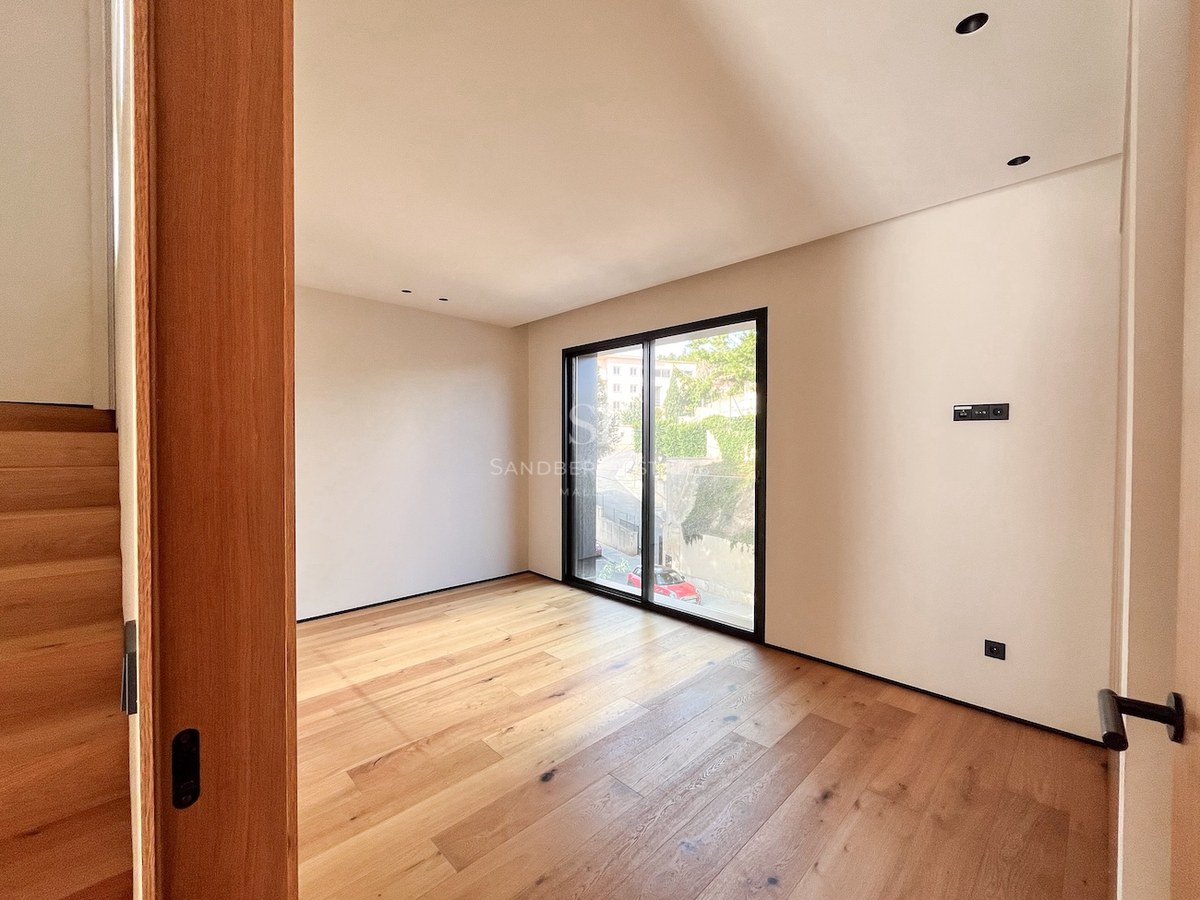 Helles Schlafzimmer mit Eichenholzboden, cremefarbenen Wänden und großem Fenster mit schwarzem Rahmen.