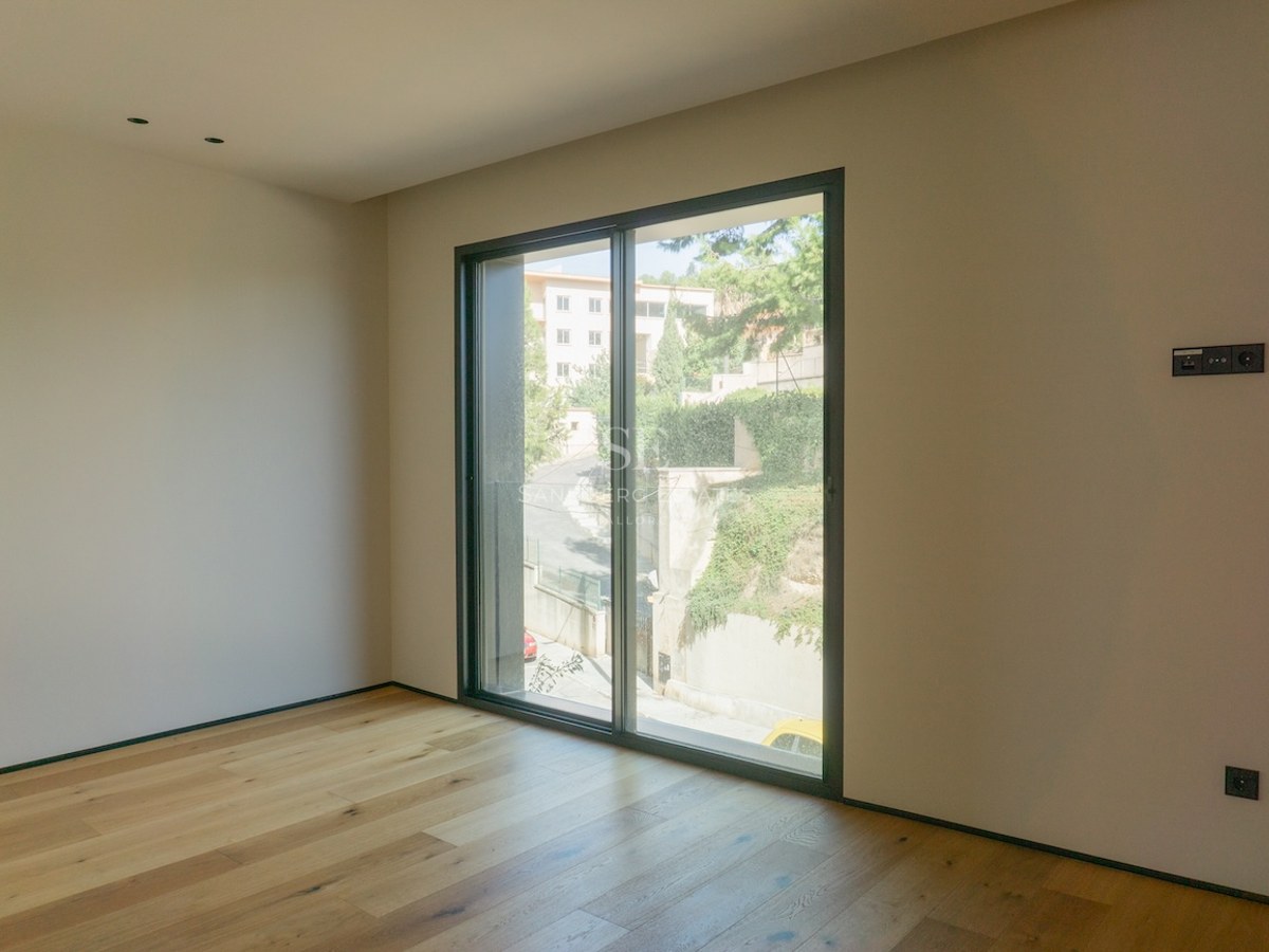 Empty modern bedroom featuring wide-plank oak floors, white walls, and a large sliding glass door.