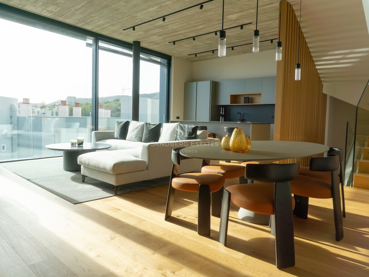 Heller, offener Wohnraum mit bodentiefen Fenstern, grauem Sofa, Holzesstisch und Sichtbetondecke.