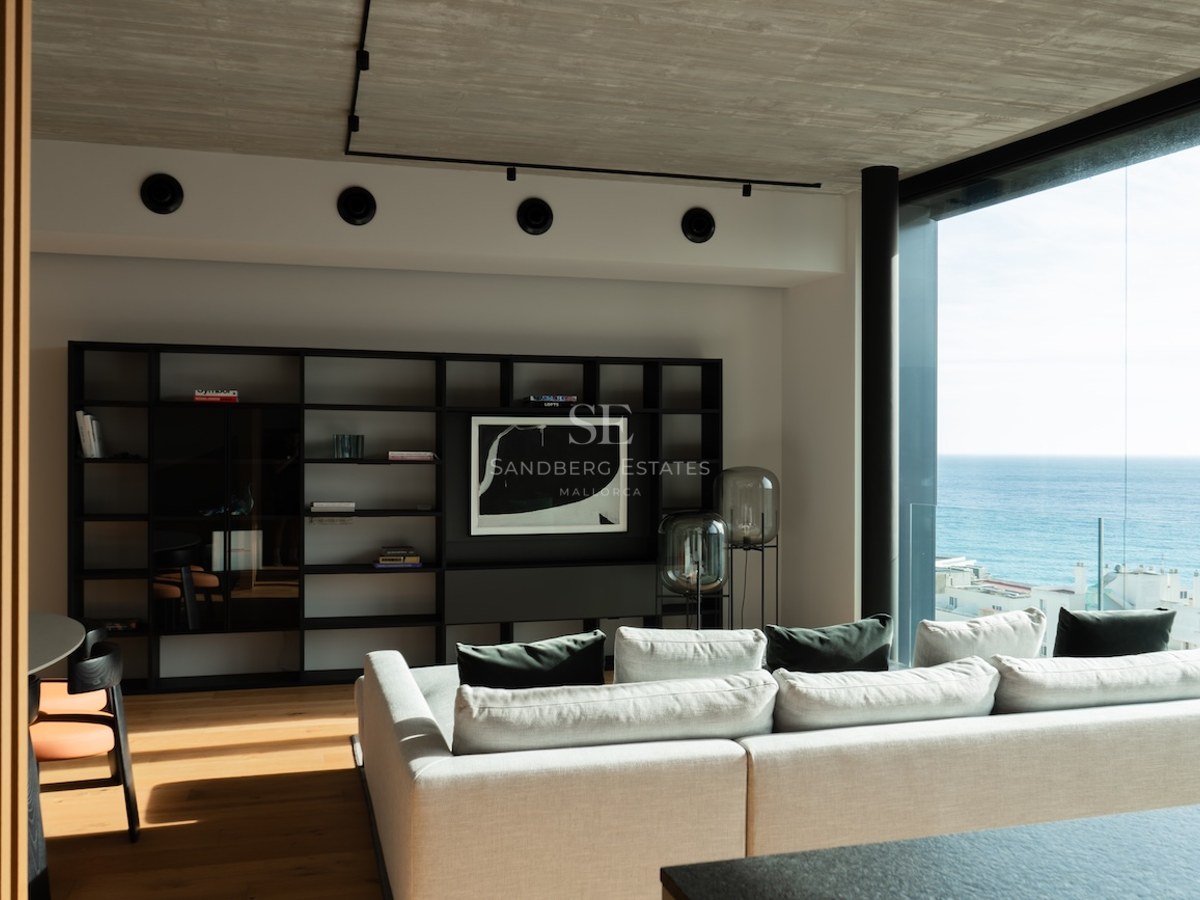 Zeitgenössisches Wohnzimmer mit bodentiefen Fenstern zum Meer, Eichenparkett und einem eleganten schwarzen Regal.