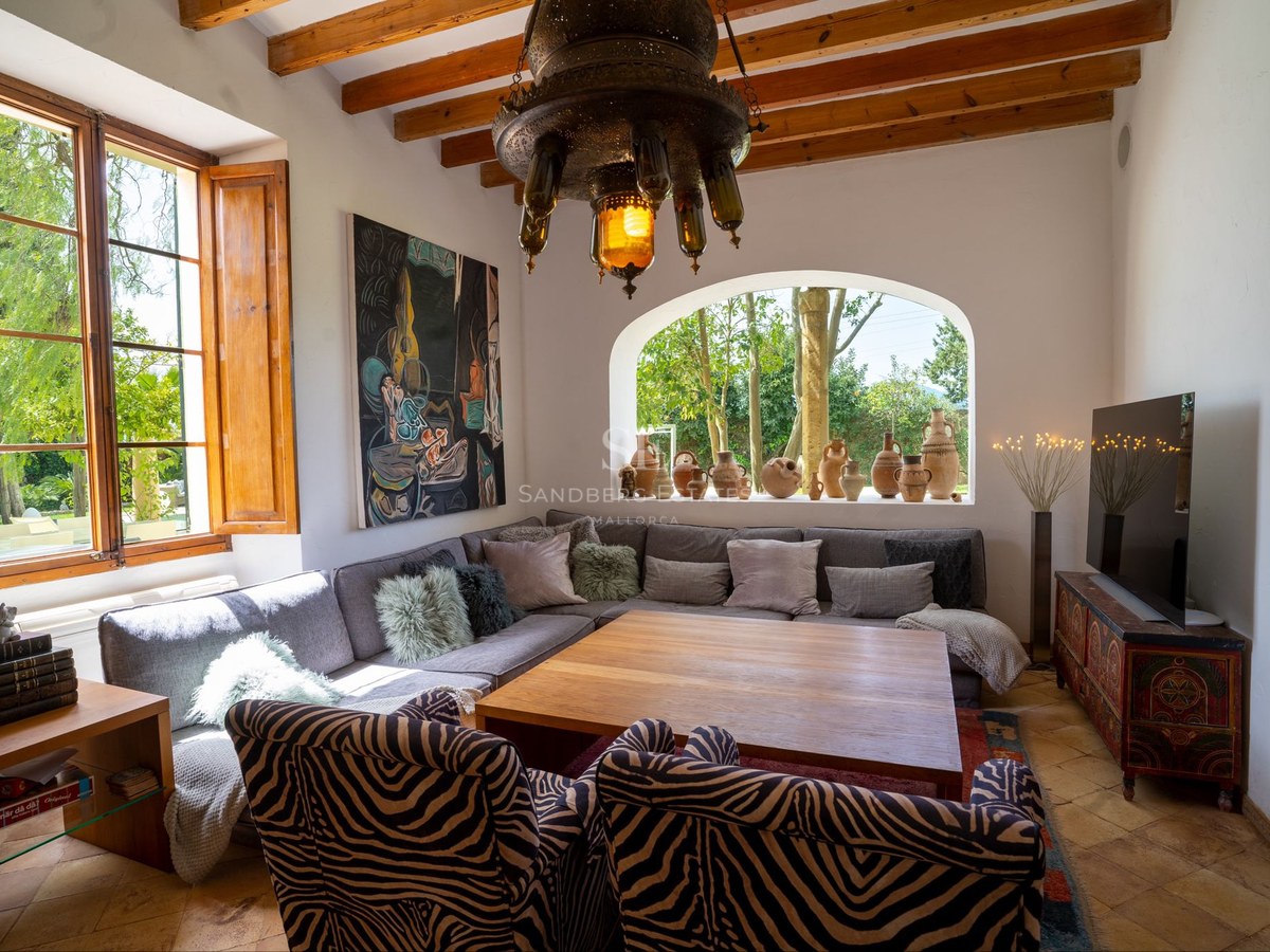 Salón acogedor con vigas de madera vistas, ventana en arco, sofá rinconera y sillones con estampado de cebra.
