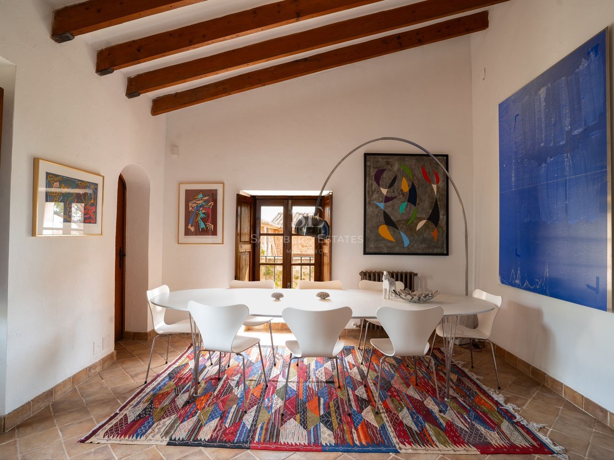 Mesa de comedor blanca con sillas de diseño bajo techos de vigas de madera y suelo de terracota tradicional.