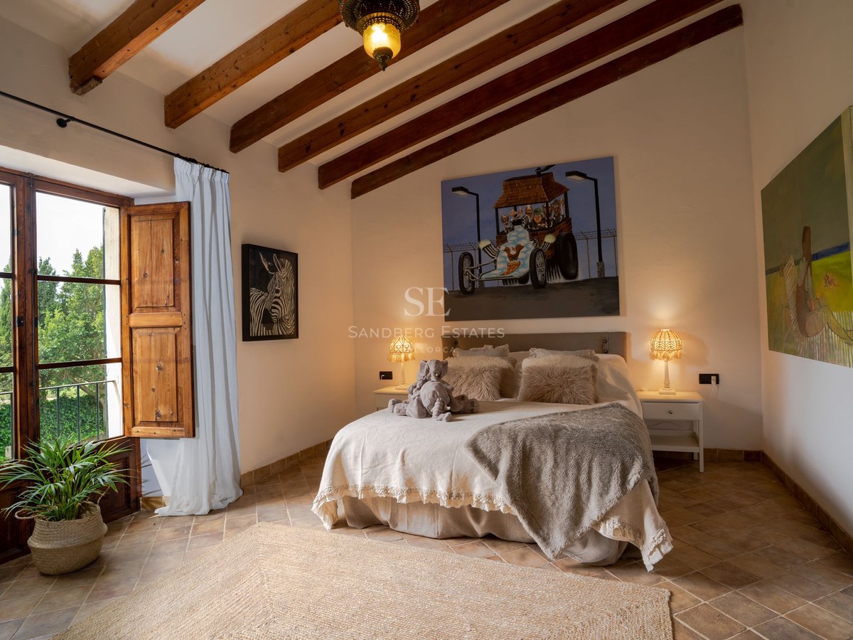 Dormitorio con vigas vistas de madera, suelo de terracota y cama doble con luz cálida y decoración acogedora.