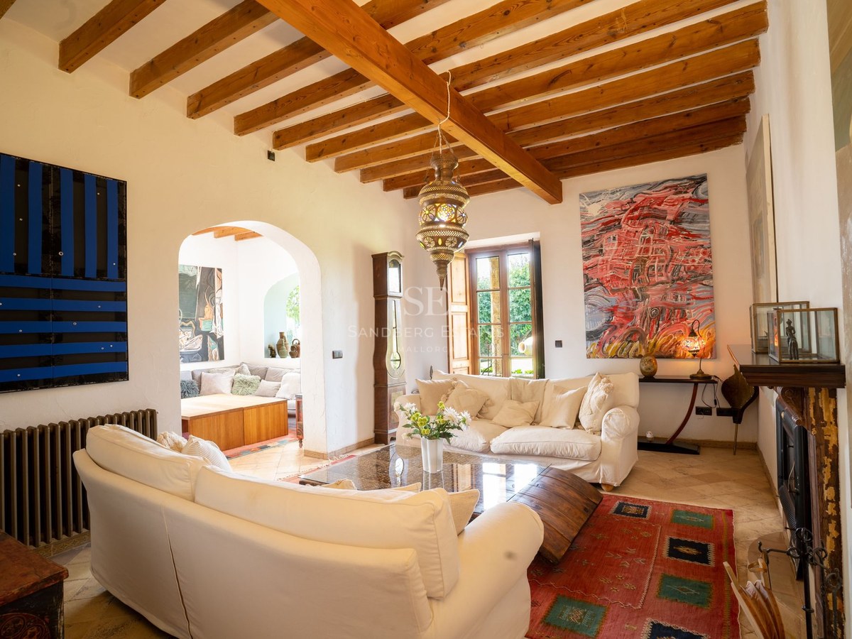 Salón con sofás blancos, techos altos de vigas de madera y una lámpara tradicional en una villa mediterránea.
