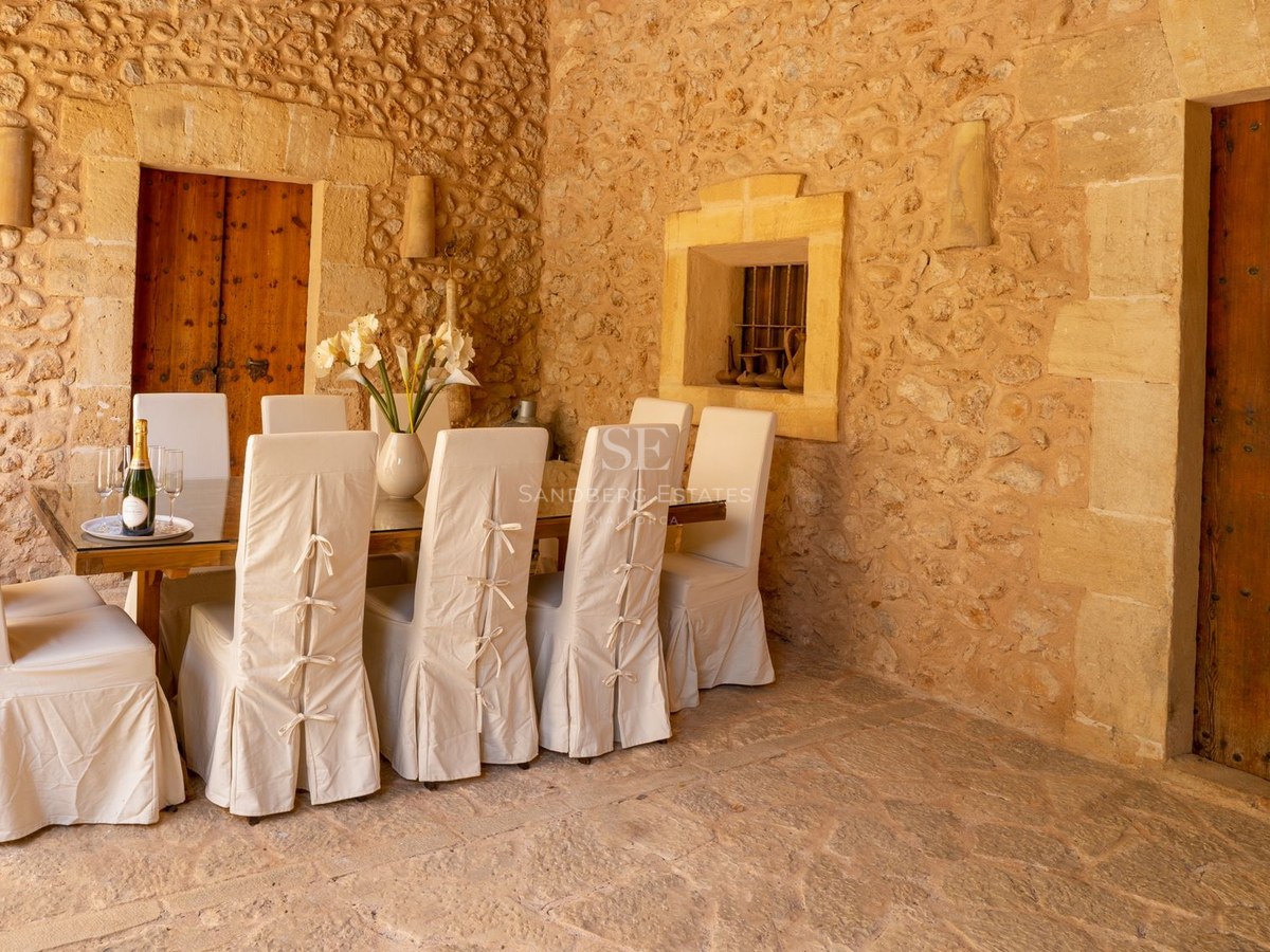 Comedor con paredes de piedra vista, mesa de madera y sillas con fundas de lino blanco.