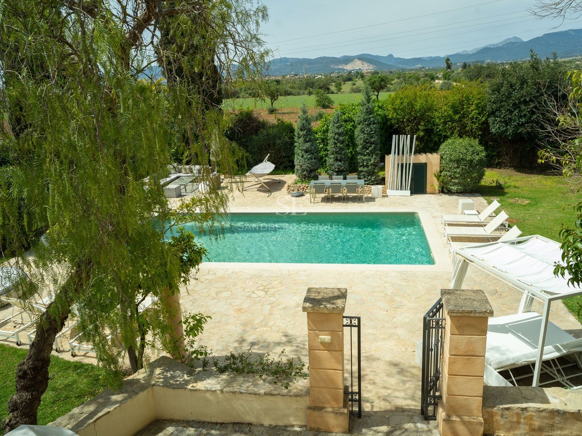 Piscina rectangular turquesa rodeada de terraza de piedra y colinas verdes al fondo.