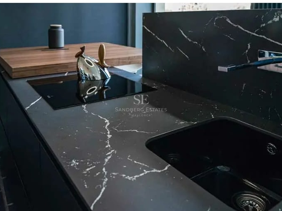 Close-up of a black marble kitchen island featuring an integrated sink, induction hob, and wooden breakfast bar.