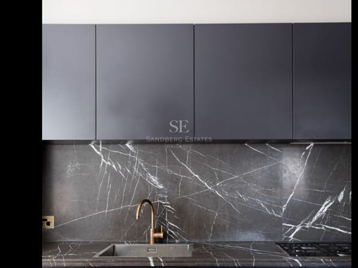 Close-up of a modern kitchen featuring a veined marble backsplash, brass faucet, and black cabinetry.