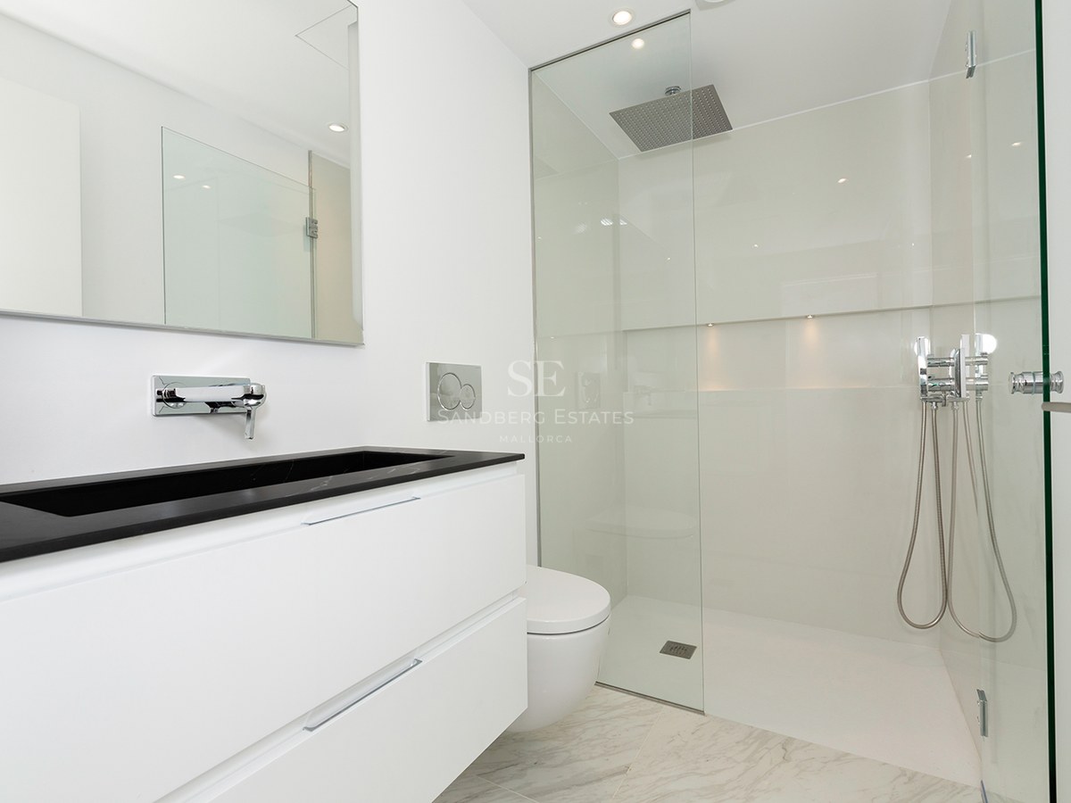 Clean white bathroom featuring a walk-in glass shower, black stone vanity, and marble-effect floor tiles.