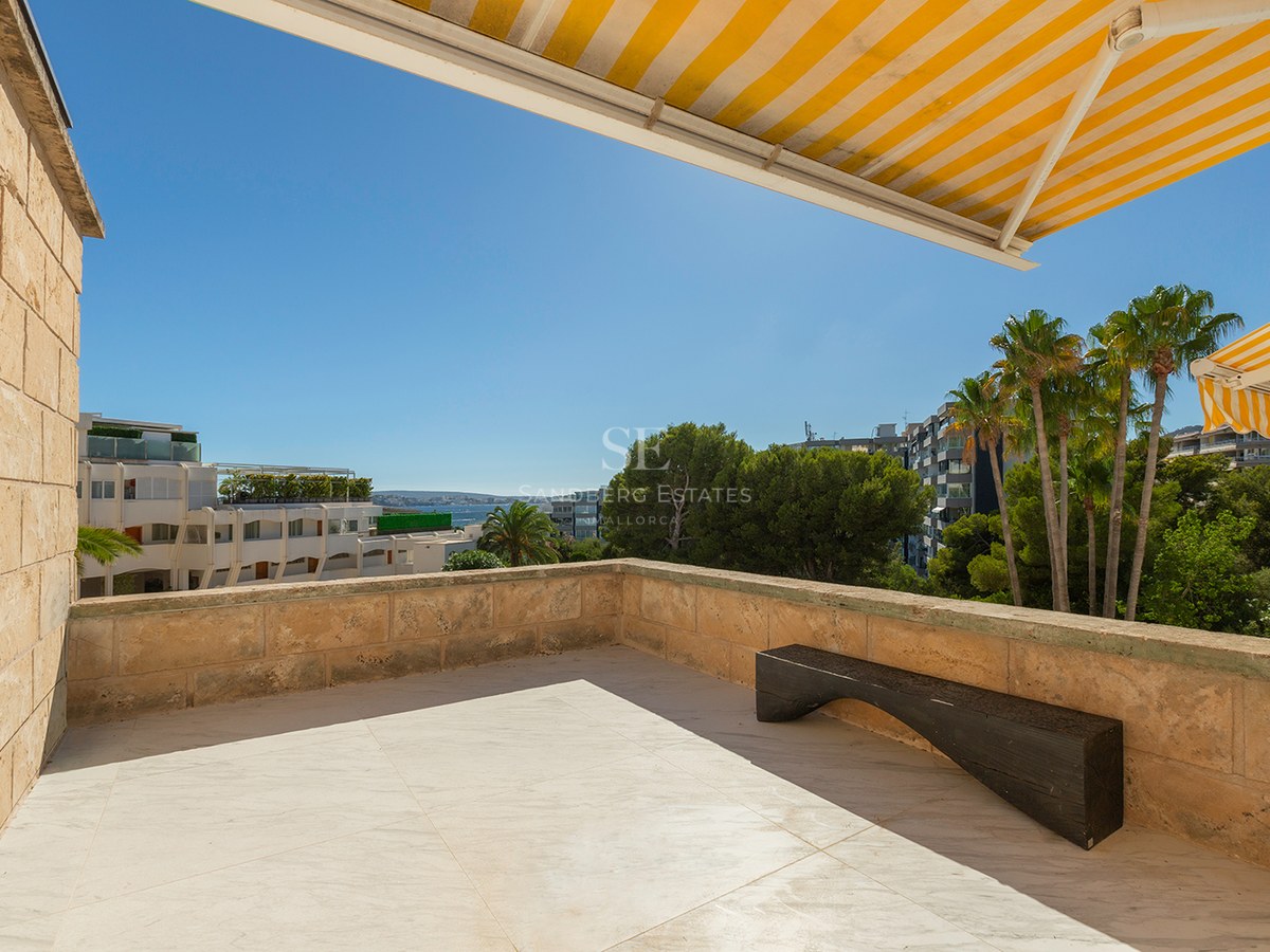 Spacious marble terrace featuring natural stone walls, a minimalist wooden bench, and yellow striped awnings.