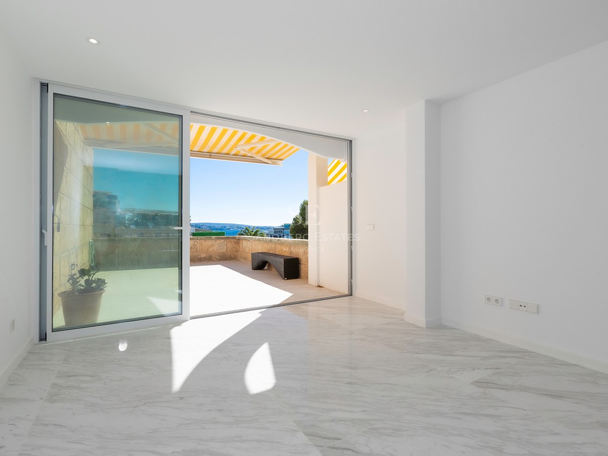 Bright empty room with white marble floors and a large sliding glass door opening to a sunny stone terrace.