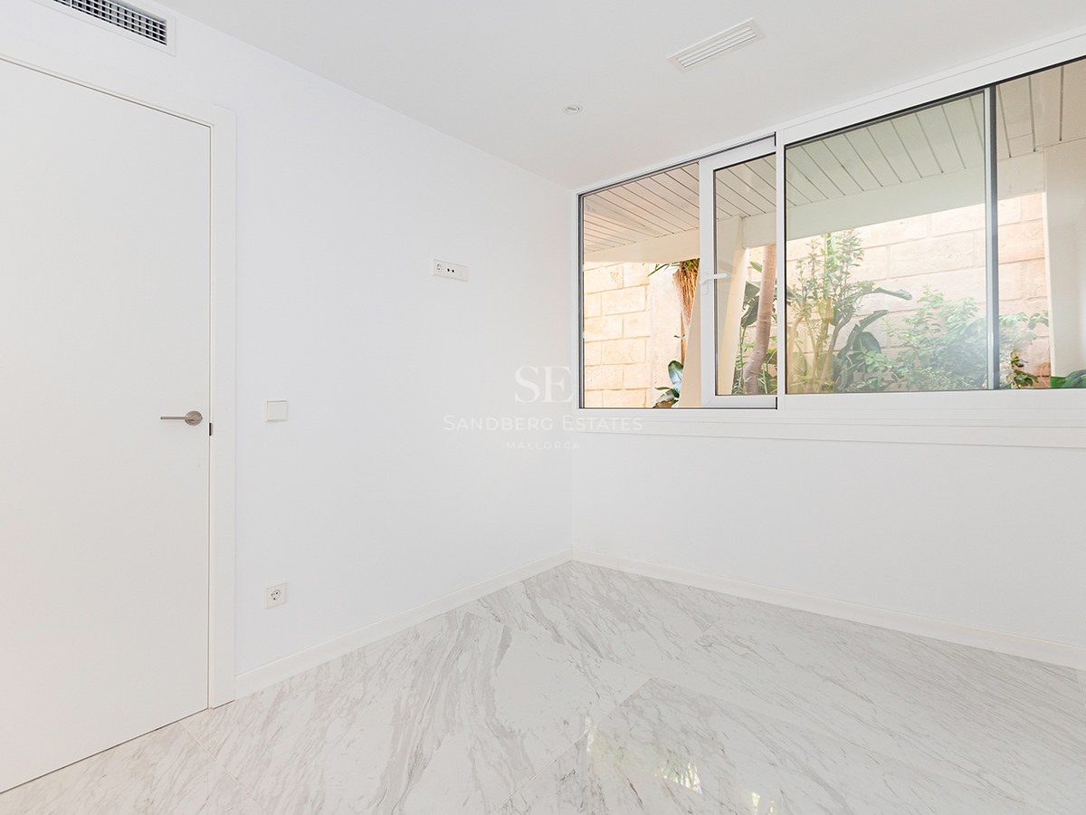 Empty room with white walls, polished marble floor, and a large sliding window overlooking outdoor greenery.