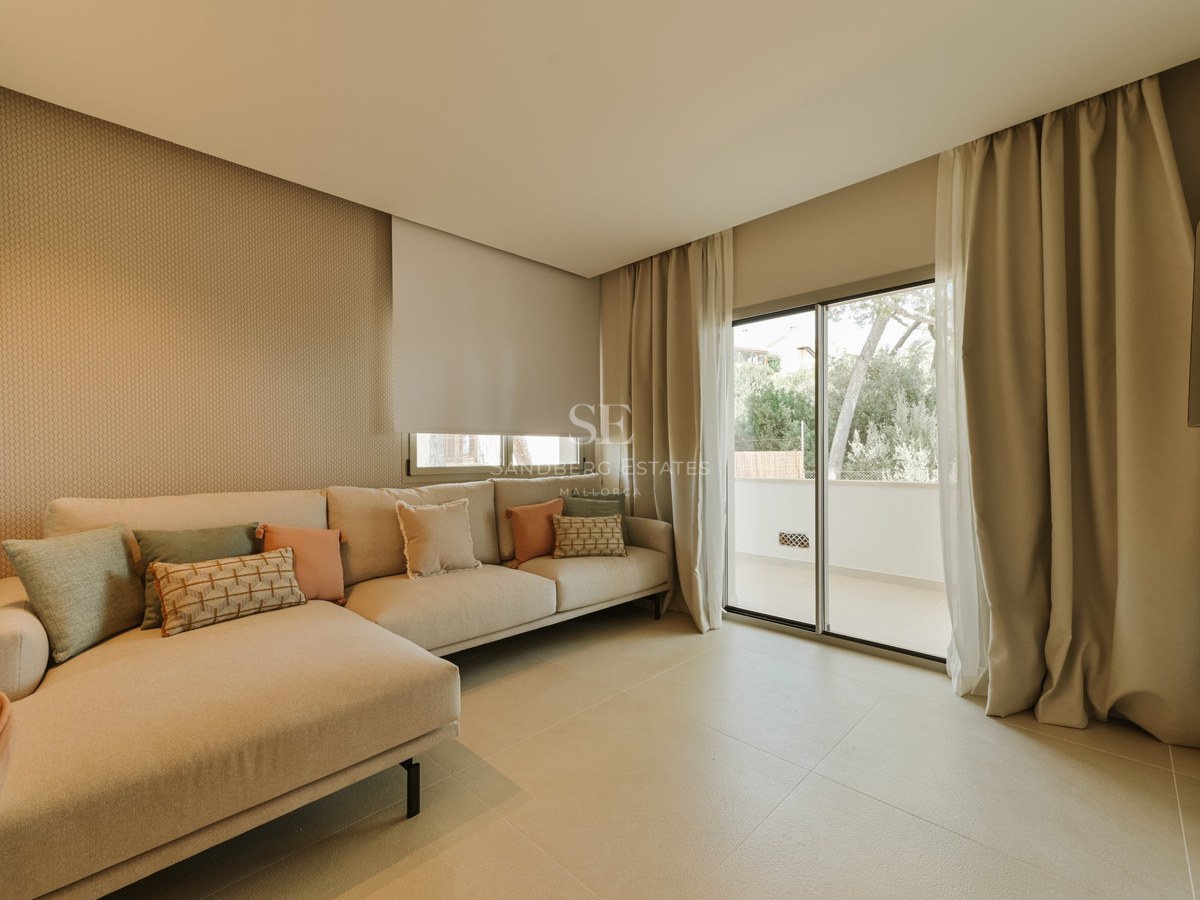 Salón moderno con sofá rinconera neutro, cojines en tonos tierra y grandes ventanales correderos hacia una terraza.