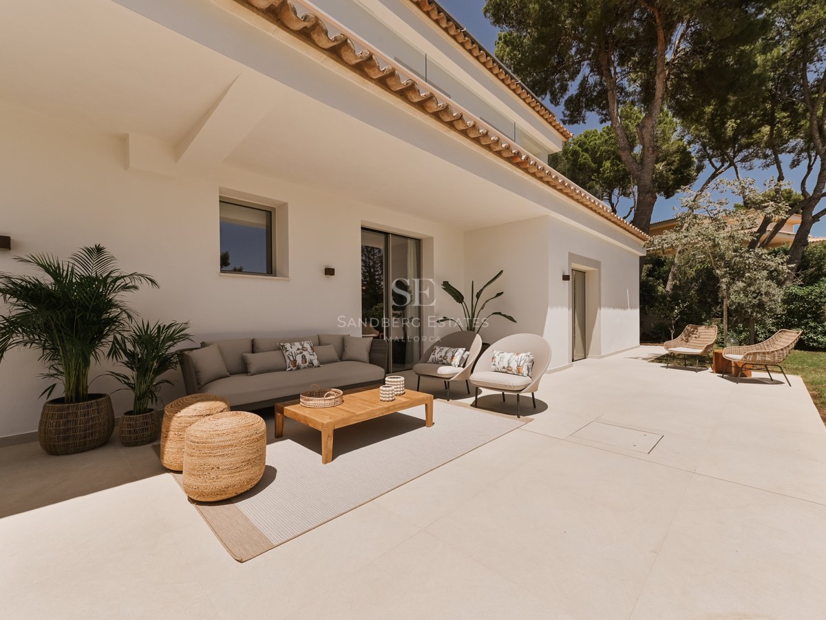 Terraza cubierta con sofá contemporáneo, mesa de madera y pufs de mimbre sobre suelos de piedra clara.