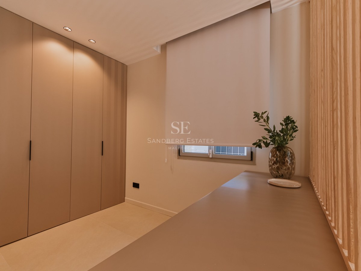 Dormitorio minimalista con armarios empotrados color topo, ventana con estor blanco y una encimera elegante.