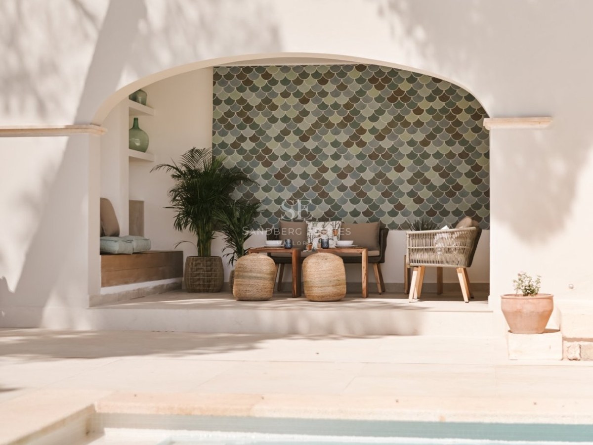 Piscina de lujo con escaleras integradas frente a una terraza cubierta con arcos y muebles de mimbre.