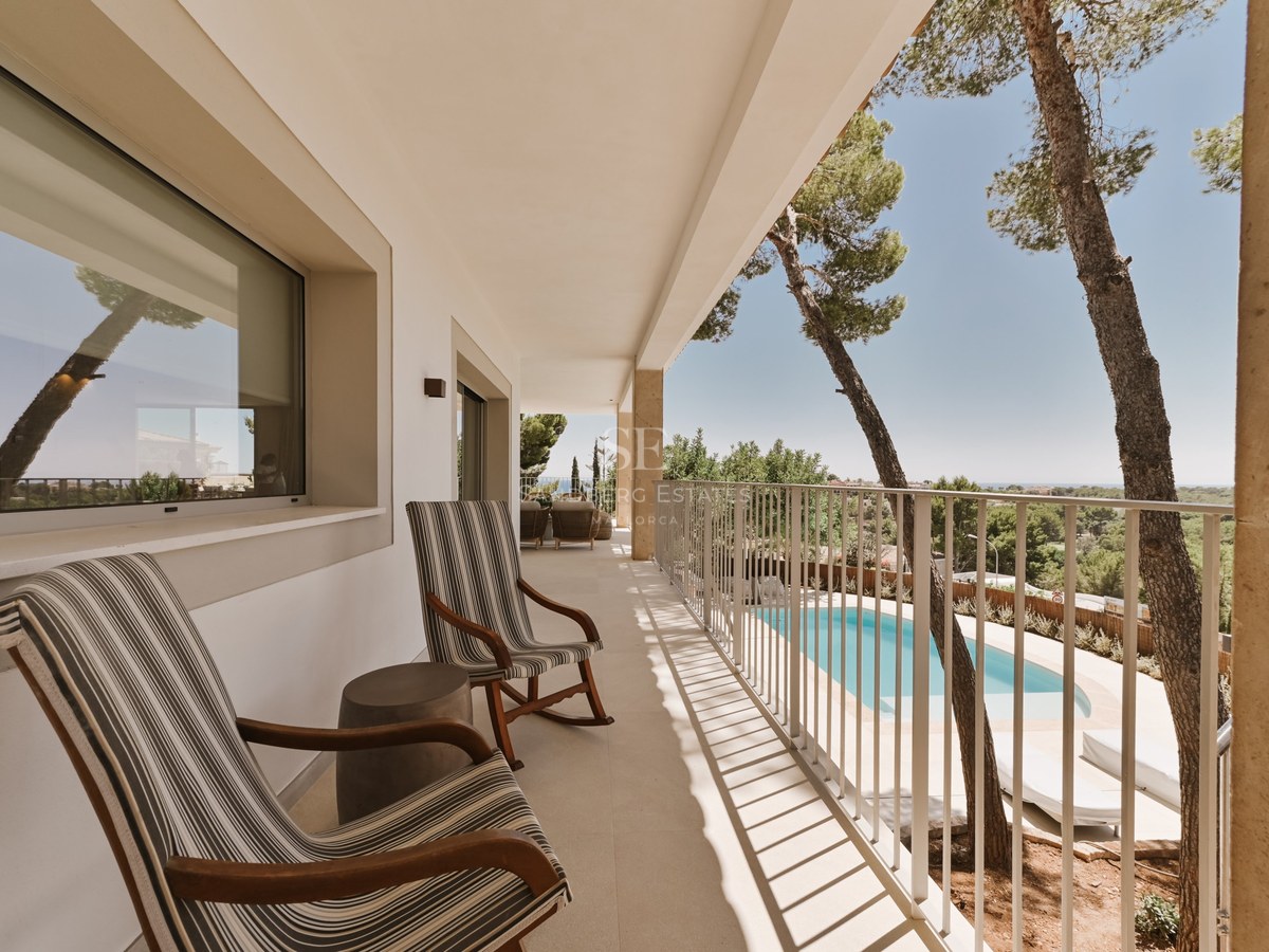Terraza blanca cubierta con dos mecedoras de rayas con vistas a una piscina privada y pinos mediterráneos.
