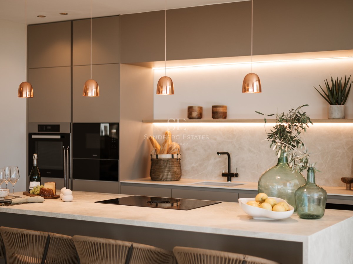 Cocina moderna con armarios color topo, salpicadero de mármol, lámparas de cobre e isla con taburetes.