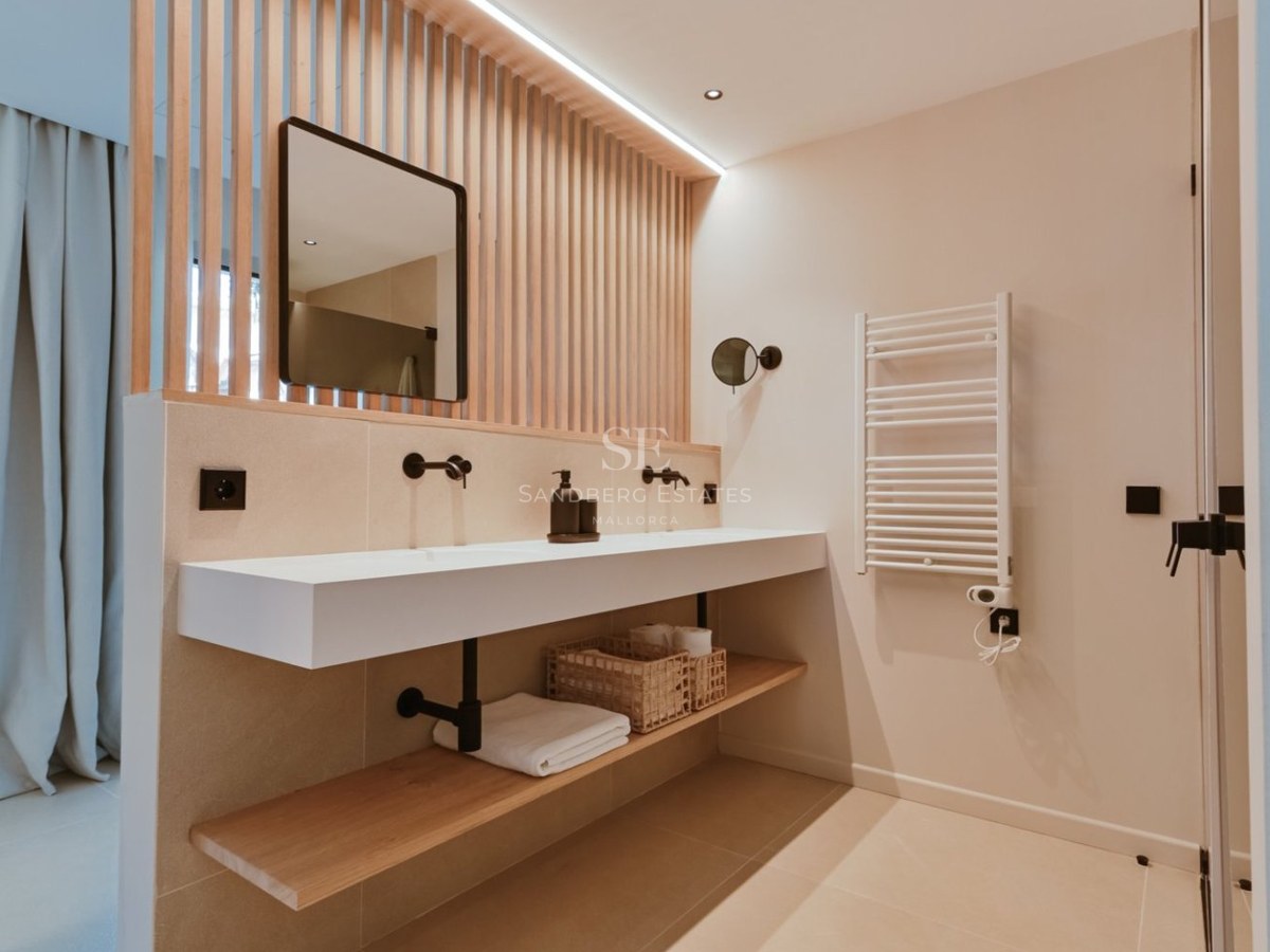 Baño moderno con lavabo suspendido blanco, grifería negra mate y panel de listones de madera verticales.