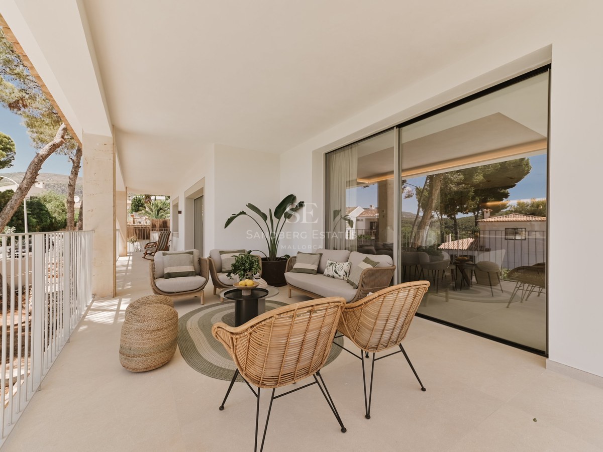 Terraza cubierta moderna con sillones de mimbre, sofá beige y amplios ventanales correderos que reflejan el exterior.