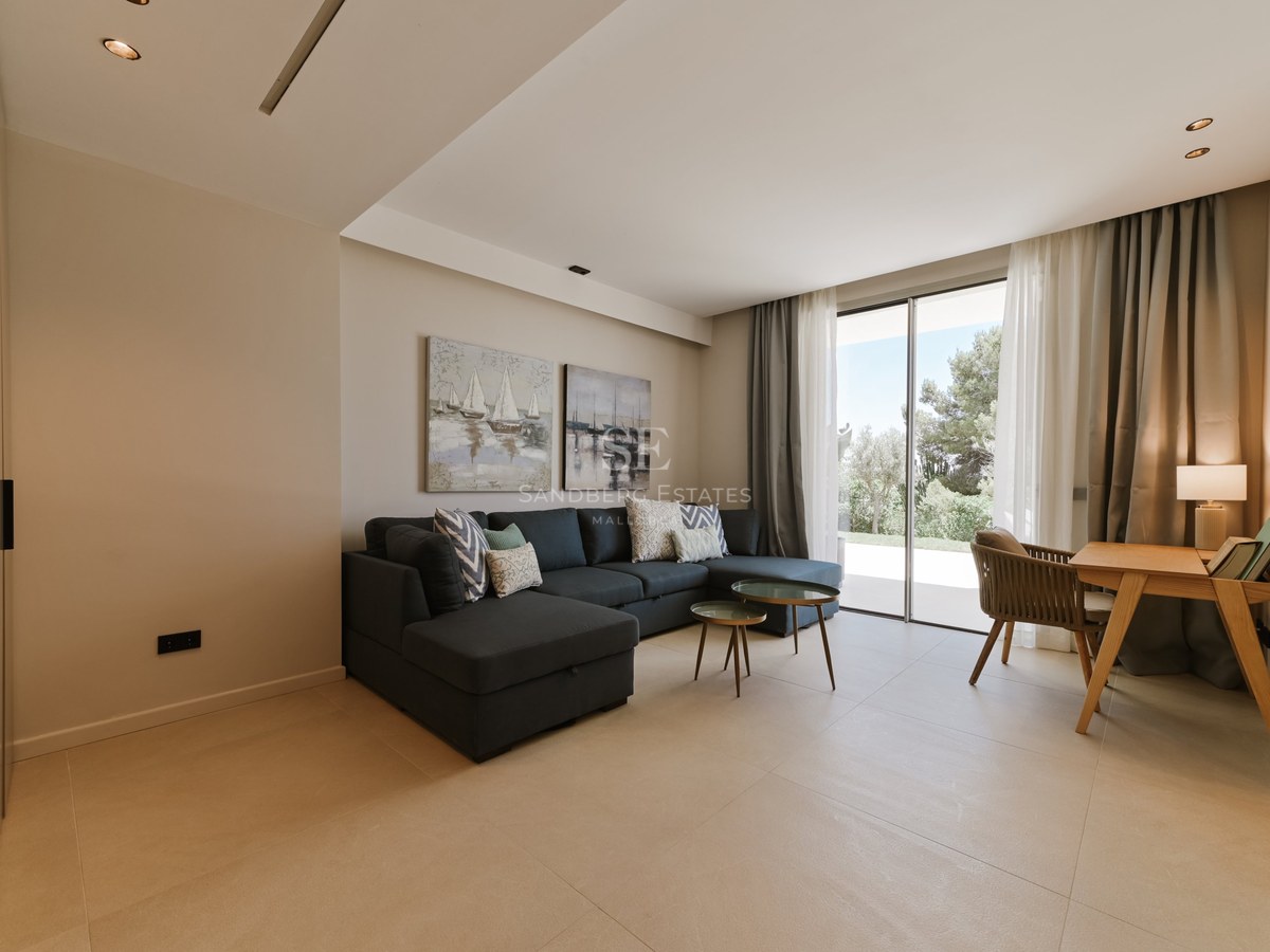 Salón moderno con sofá modular gris oscuro y ventanales de suelo a techo con vistas a la terraza.