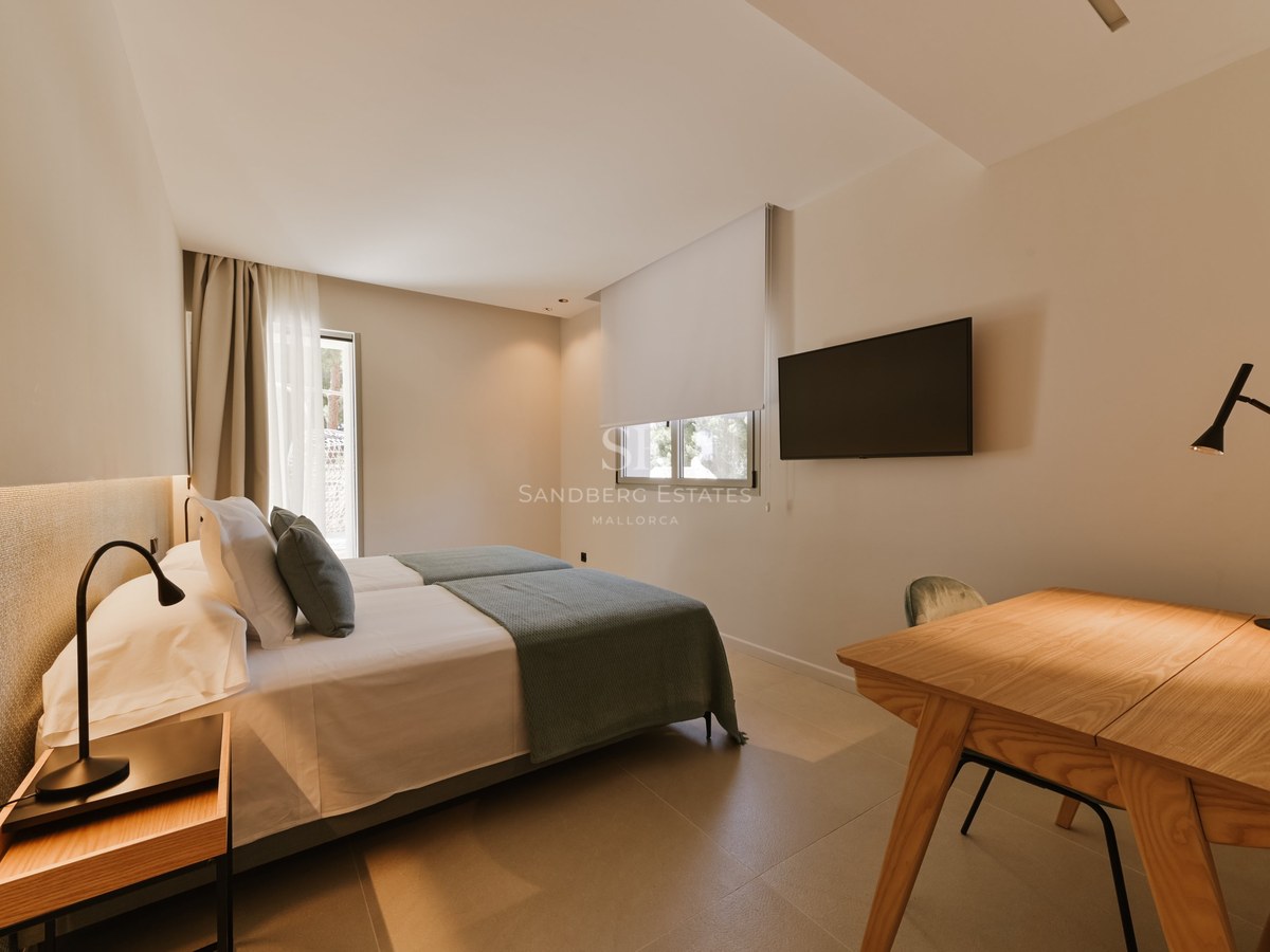 Dormitorio minimalista con camas gemelas, ropa de cama gris, escritorio de madera y televisor de pared.