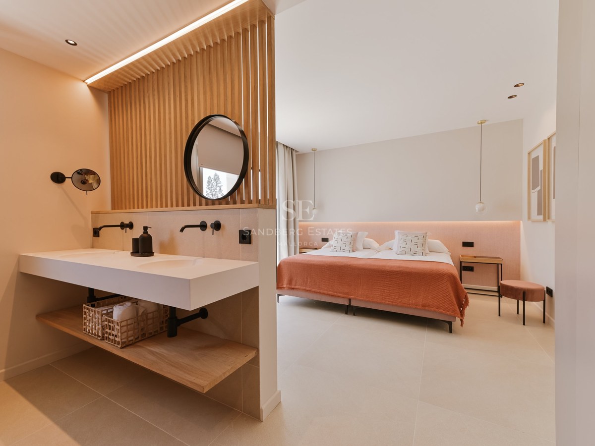 Dormitorio con separador de listones de madera entre el lavabo doble y una cama con textiles terracota.