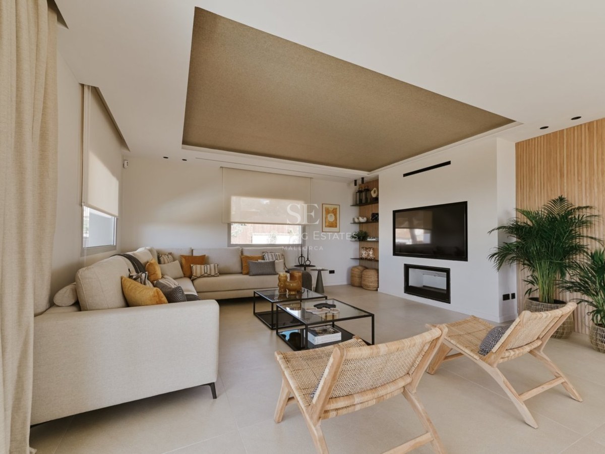 Salón contemporáneo con sofá en L color crema, sillas de madera, mesas de cristal y chimenea empotrada.