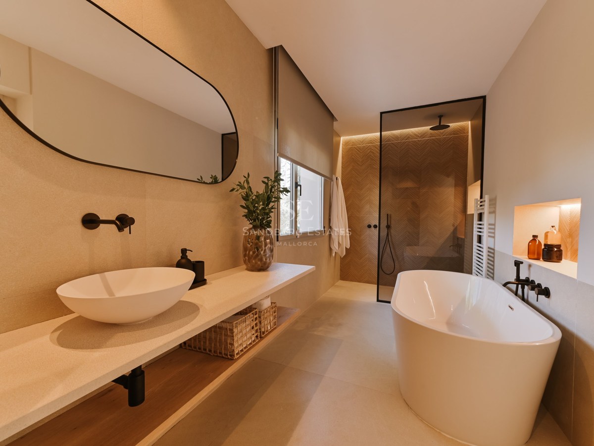 Baño moderno con bañera blanca exenta, encimera flotante de piedra y ducha de obra con mampara de cristal.
