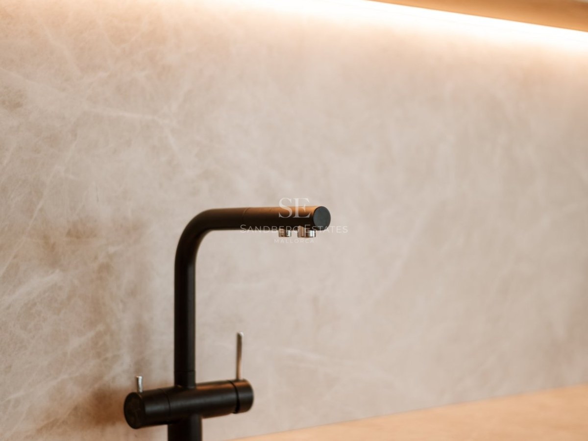 Grifo negro mate sobre salpicadero de piedra beige con iluminación LED integrada en una cocina de lujo.