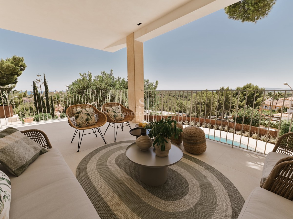 Terraza de piedra cubierta con sillones de mimbre, alfombra ovalada y mesa redonda con vistas a un parque y piscina.