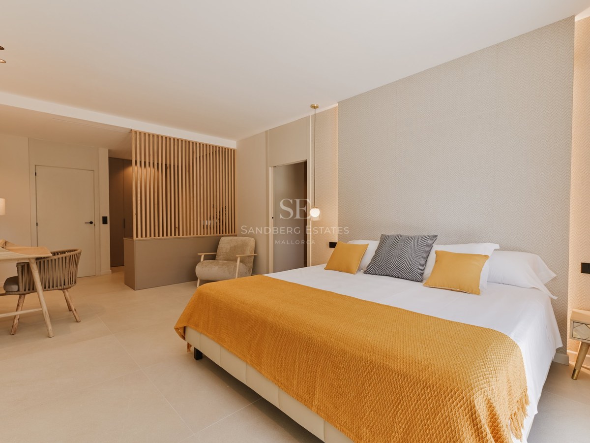 Dormitorio moderno con cama doble, manta ocre y divisor de ambientes de listones de madera en tonos neutros.