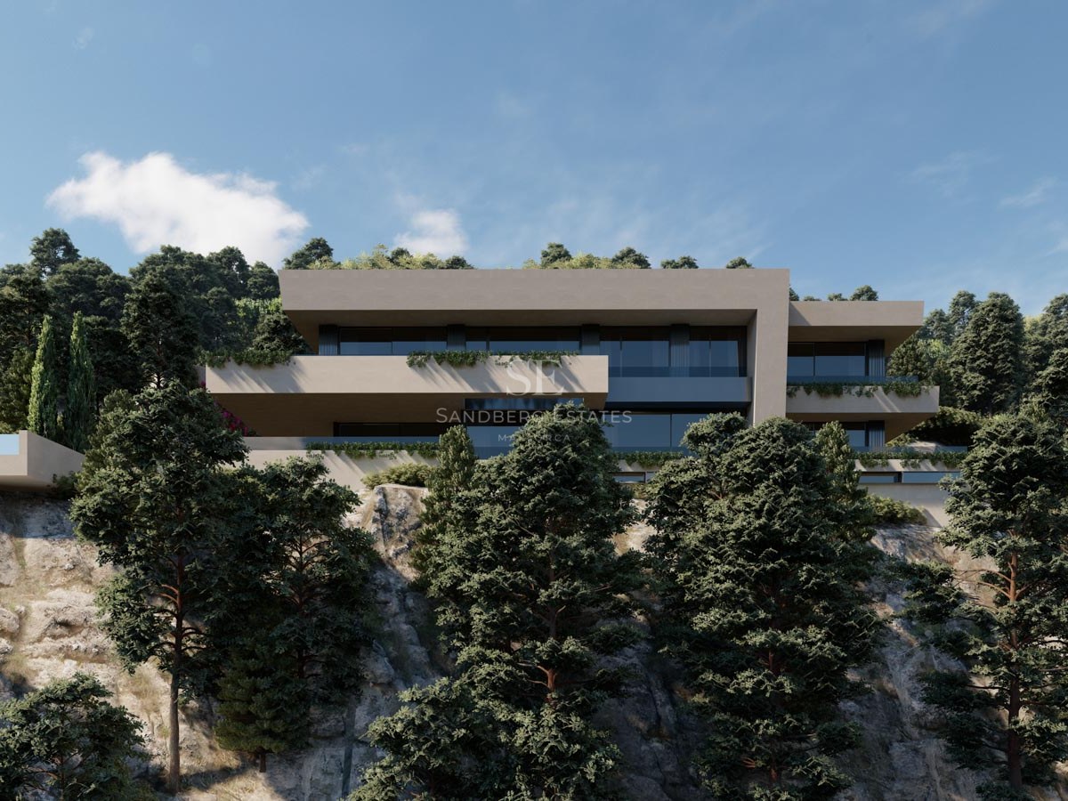 Modern flernivåvilla med stora glaspartier inbyggd i en klippa omgiven av gröna tallar.