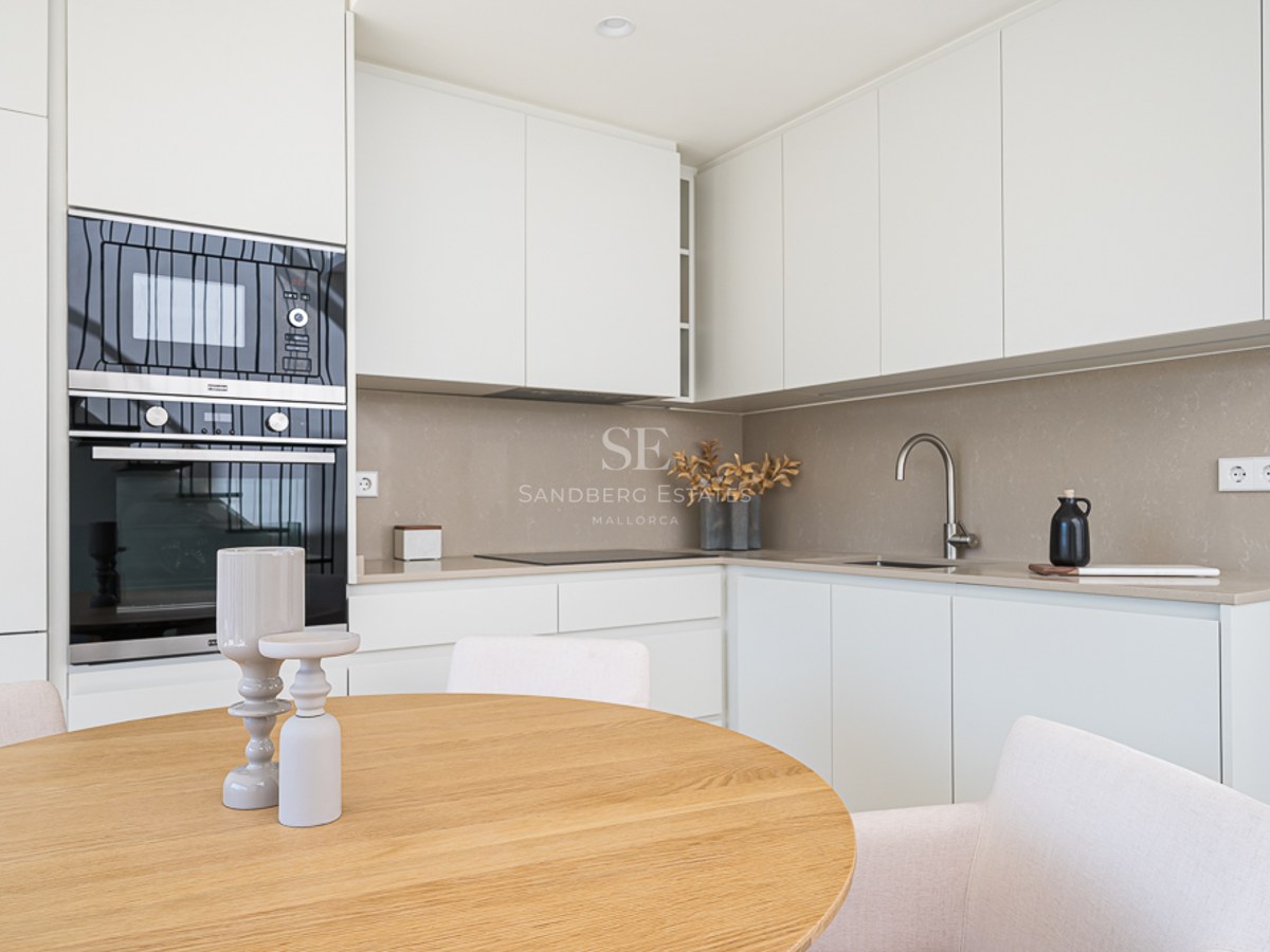 Cocina blanca moderna con encimera de cuarzo, electrodomésticos integrados y mesa de comedor redonda de roble.