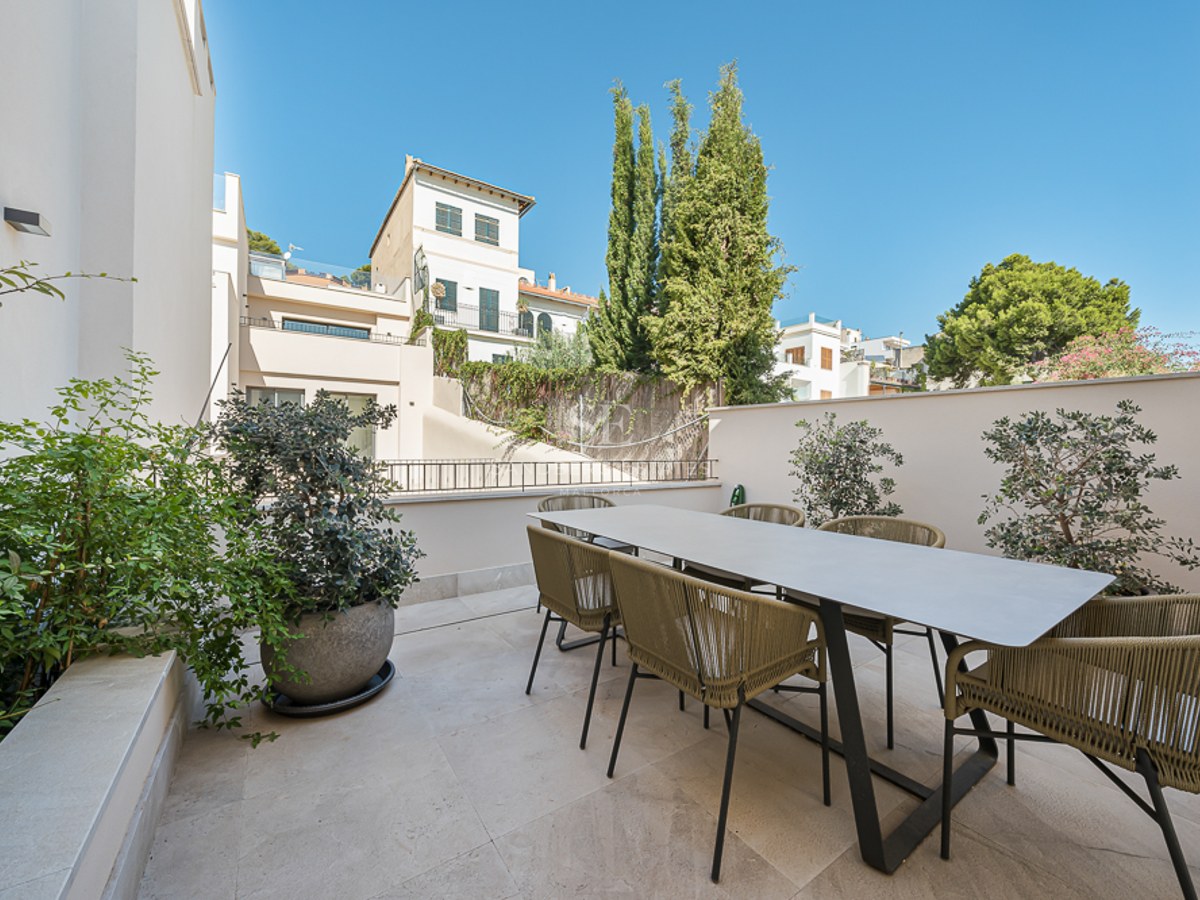 Terraza exterior contemporánea con mesa de comedor grande y seis sillas de cuerda trenzada sobre suelo de piedra clara.